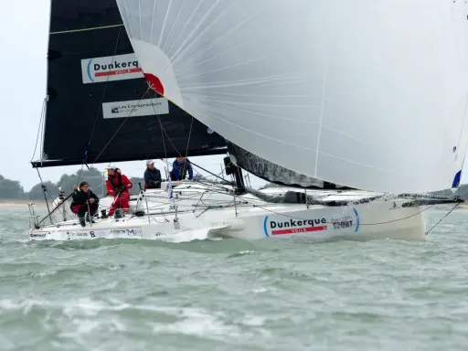 Un voilier "Dunkerque Voile" navigue avec un équipage concentré. Eliott Coville, peut-être à bord, profite de la course.