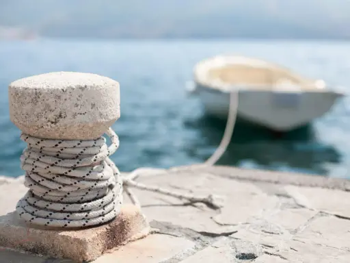 Un cordage est enroulé autour d'une borne en pierre sur un quai, prêt pour le prochain pendille bateau.