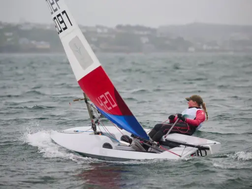 Jeune navigatrice en dériveur **tabur 320**, voile rouge et bleue, naviguant sur une mer agitée.