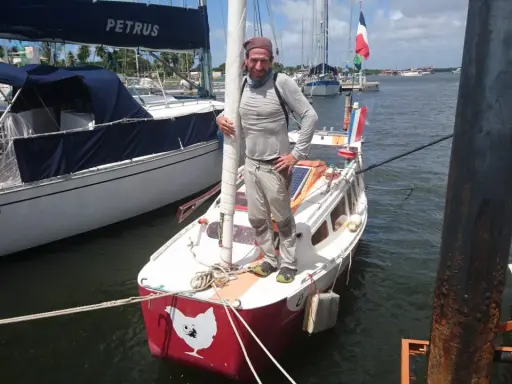Yann Quenet, prêt pour l'aventure avec son baluchon, pose sur son voilier orné d'une poule.