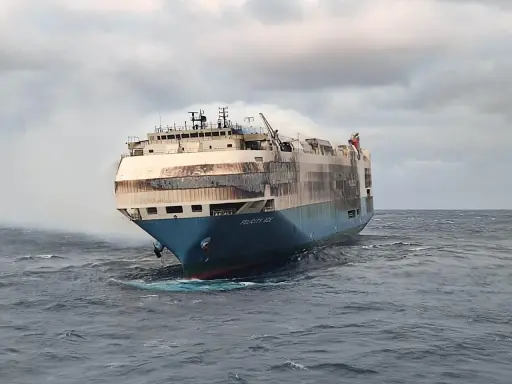 Le cargo Felicity Ace, en feu, dérive sur une mer agitée. De la fumée s'échappe de ses ponts supérieurs.