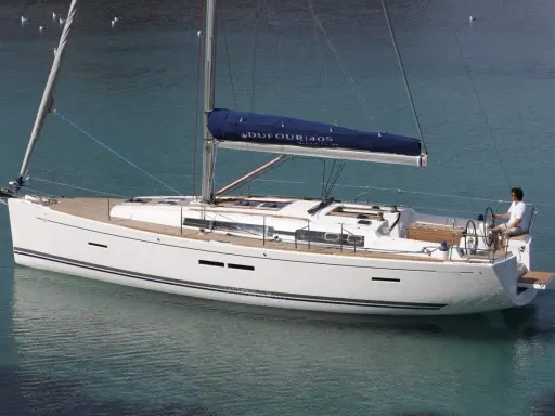 Un voilier blanc Dufour 405 Grand Large navigue sur une eau turquoise. Un homme est au poste de barre.