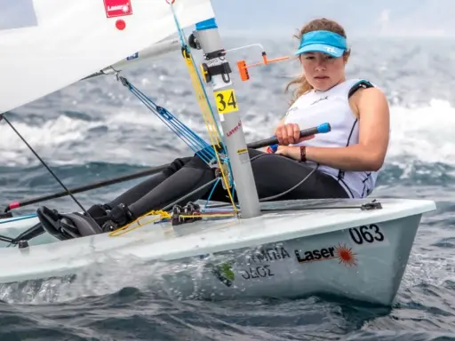 Jeune femme concentrée naviguant en deriveur solo, le bateau #063 fend les vagues.