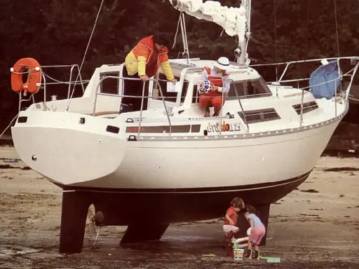 Le voilier "Évasion 29" échoué sur la plage, avec deux enfants jouant à ses pieds et deux adultes à bord.