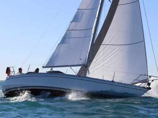 Un voilier Jeanneau Symphony navigue sur une mer agitée, ses voiles blanches gonflées par le vent. Un avis positif pour ce bateau.