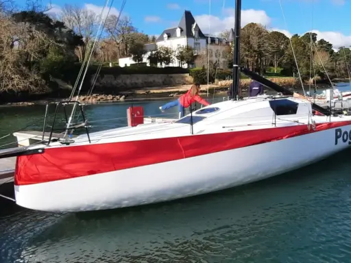 Le voilier Pogo RC, blanc et rouge, est amarré à un ponton. Une personne en blouson rouge est à bord.