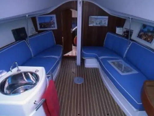 Intérieur du JOD 35, avec banquettes bleues, évier en inox et parquet en bois. Prêt pour une nouvelle aventure en mer.