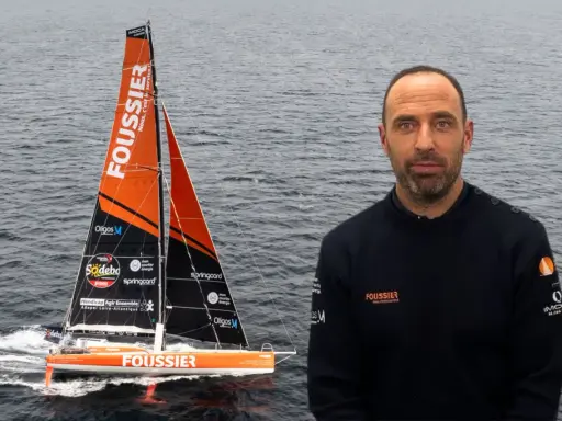Sébastien Marsset, skipper du voilier Foussier, prêt pour la course. Le bateau orange et noir fend les vagues.