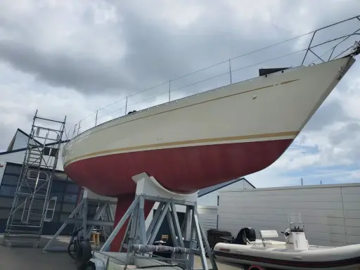 Le nouveau bateau de Jean Le Cam, un voilier blanc et rouge, est sur des supports à côté d'un atelier.