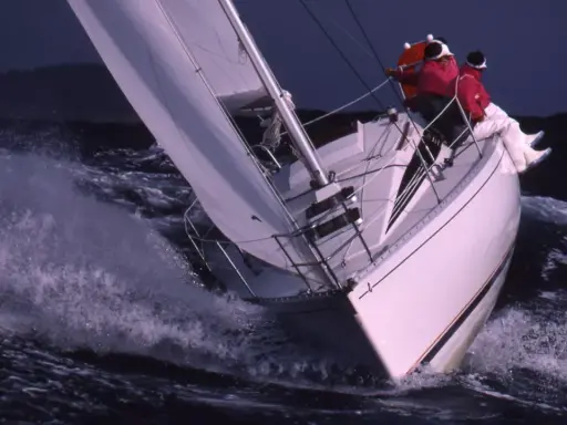 Voilier blanc fendant les vagues, deux personnes en ciré rouge. Une scène de navigation intense, digne des premiers 285 avis.