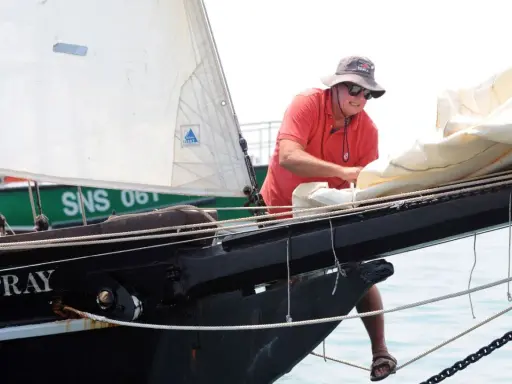 Un homme, Guy Bernardin, ajuste les voiles du Spray, un voilier historique, par une journée ensoleillée.