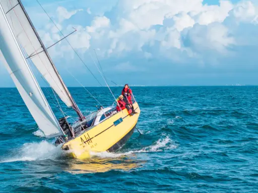 Un voilier jaune fend les vagues bleues, ses voiles blanches gonflées par le vent. L'équipage profite de cette belle journée pour faire la voile.