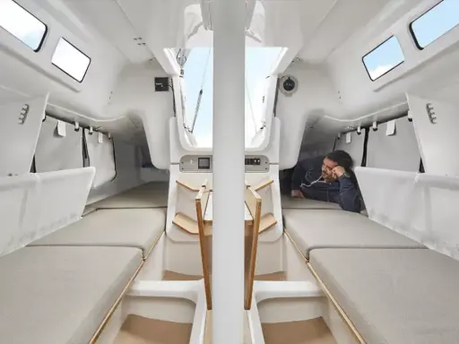 L'intérieur du voilier, premier 27, offre des couchettes confortables et un espace de vie lumineux. Un homme se repose, profitant du calme.
