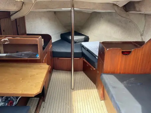 L'intérieur du Jeanneau Brio offre un espace de vie confortable avec des banquettes en tissu noir, une table en bois et des boiseries chaleureuses.