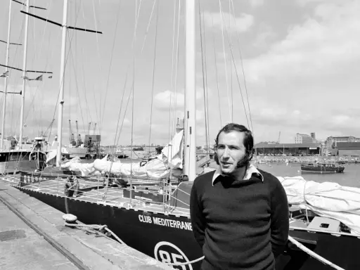Un homme pose devant le voilier "Club Mediterranee". Ce navigateur célèbre semble prêt pour une nouvelle aventure maritime.