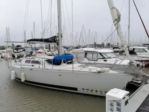 Un voilier blanc, "PEELIN", est amarré dans un chantier naval. D'autres bateaux sont visibles en arrière-plan.