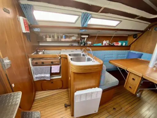 Cuisine de voilier avec cuisinière, évier double, banquette bleue et table en bois. Un radiateur est visible. 312 avis gib sea.