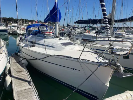 Bavaria 32, un voilier blanc avec une voile bleue, amarré dans un port. Avis sur ce modèle de bateau.