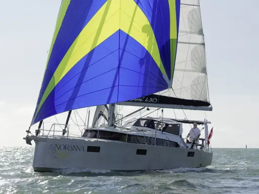 Le voilier "Noranna" L430 navigue sur une mer agitée, sa grand-voile aux couleurs vives bleu et jaune captant le vent.