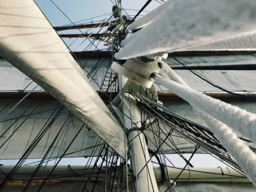 Vue en contre-plongée des voiles d'un voilier, avec le gréement dormant complexe et les cordages épais.