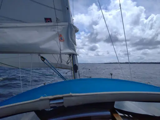 Vue depuis un voilier, avec la liste des voiles d'un bateau gonflées par le vent. La mer est agitée sous un ciel nuageux.
