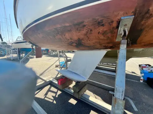 Vue du dessous d'un voilier sur bers. Le safran est visible, prêt pour l'étape 22 de la fiche technique.