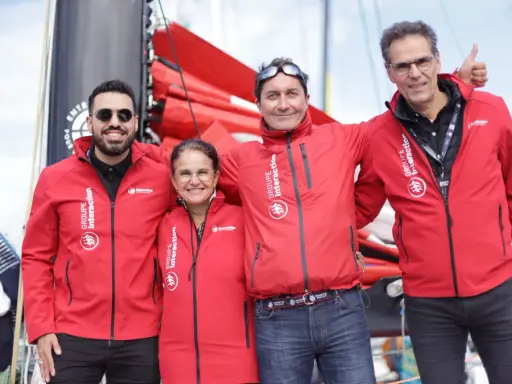 Erwan Thiboumery et trois autres personnes souriantes portent des vestes rouges du Groupe Interaction, devant un bateau.
