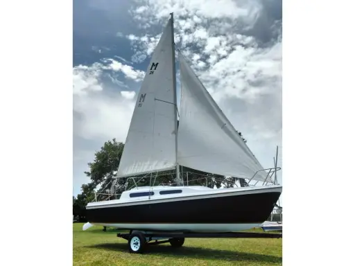 Voilier Mac Gregor 25, prêt à naviguer, avec ses voiles blanches gonflées par le vent sous un ciel nuageux.
