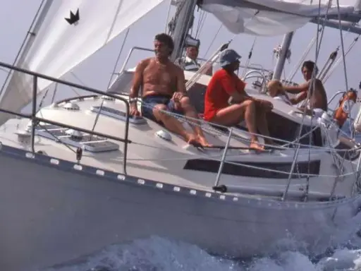 Un groupe profite d'une journée en mer sur ce qui semble être le meilleur voilier fifty, naviguant sur des eaux bleues avec des voiles blanches gonflées par le vent.