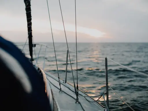 Vue depuis le pont d'un voilier insubmersible naviguant sur une mer calme au coucher du soleil.
