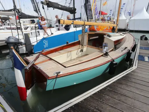 Un élégant belouga bateau, aux finitions bois et coque turquoise, est amarré à quai.