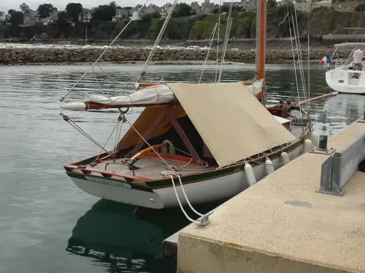 Un cotre de Carantec, "Le Vieux Gui", est amarré au port. Une autre voile blanche est visible à côté.