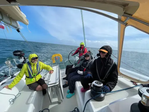 Équipage souriant sur un voilier, profitant de la navigation. Personne n'a besoin d'écoper, la mer est calme.