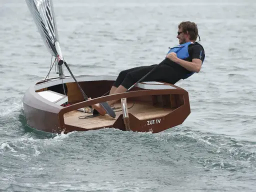 Un homme navigue sur un petit bateau en bois, le "ZUT IV", dans une mer agitée.
