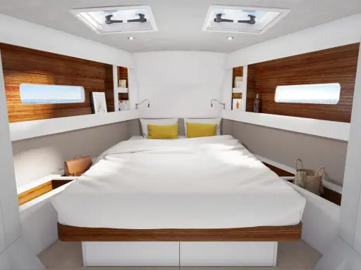L'intérieur d'un voilier 8m, avec un grand lit blanc, des coussins jaunes, des hublots donnant sur la mer et des étagères en bois.