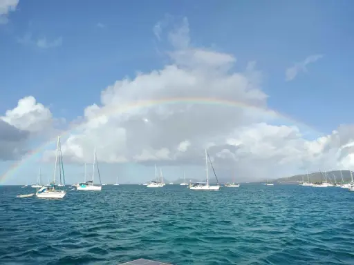 Un arc-en-ciel sur une mer bleue, parsemée de voiliers. L'appel de l'aventure : tout quitter pour vivre sur un bateau.