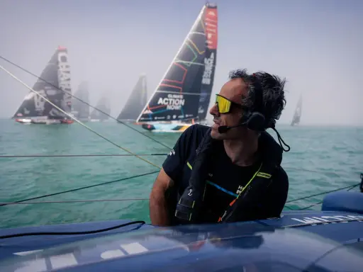 Franck Cammas, concentré, navigue en tête d'une flotte de voiliers dans le brouillard.