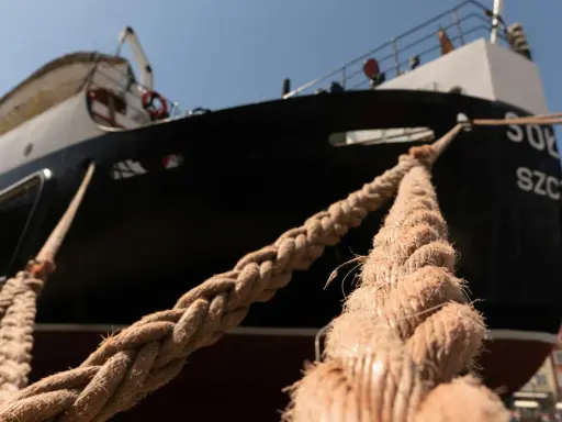 Gros plan sur des cordages épais assurant l'amarrage d'un bateau noir et blanc, avec des bâtiments colorés en arrière-plan.
