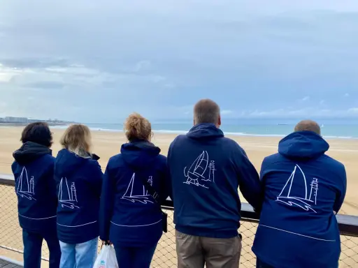 Cinq personnes portent des vestes bleues avec des voiliers dessinés. Benoit Marie et ses amis admirent la mer.