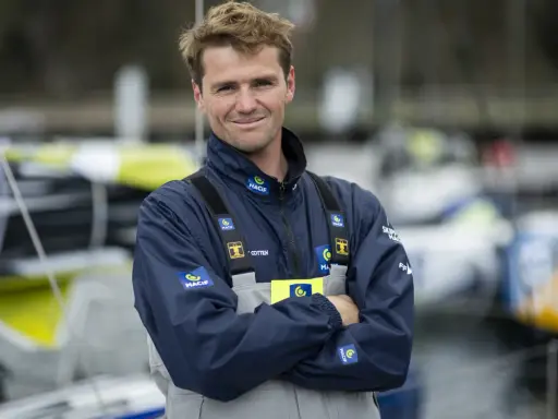 L'athlète marin Lois Berrehar, souriant, porte une veste bleue MACIF avec des logos. Derrière lui, des voiliers colorés.