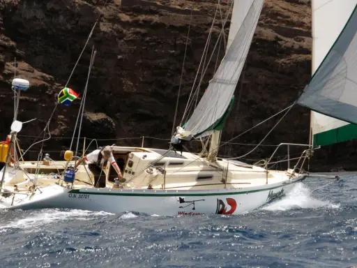 Un voilier cap horn, le "Windicator", navigue près d'une côte rocheuse. Le drapeau sud-africain flotte fièrement.