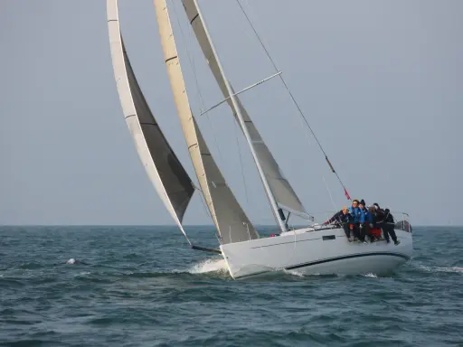 Équipage sur un voilier blanc, le foc et le génois gonflés par le vent, naviguant sur une mer agitée.