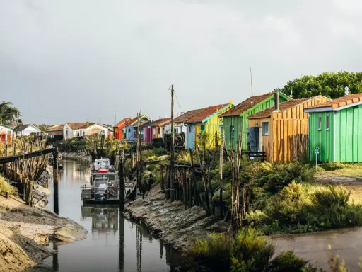 Cabanes colorées alignées le long d'un canal, un bateau amarré. Un charmant port sur l'Île d'Oléron.