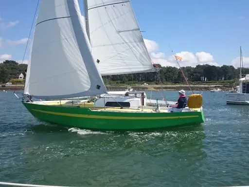 Un voilier vert vif navigue sur l'eau, avec un autre bateau à moteur en arrière-plan. Une belle journée pour une croisière, peut-être avec une dégustation d'armagnac à bord de ce bateau.
