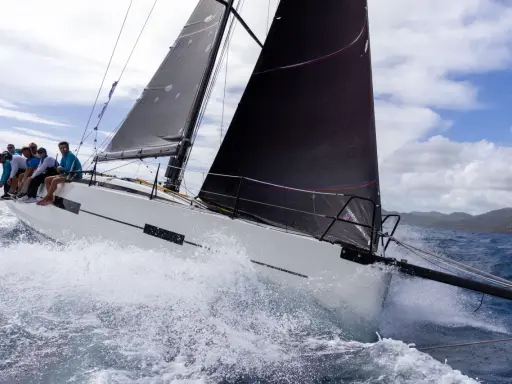 Équipage sur un voilier blanc, gery trentesaux, naviguant sur une mer agitée sous un ciel nuageux.