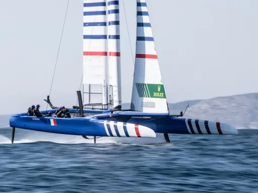 Catamaran bleu et blanc, voiles rayées, en pleine action. La **vitesse catamaran** est impressionnante, les foils hors de l'eau.