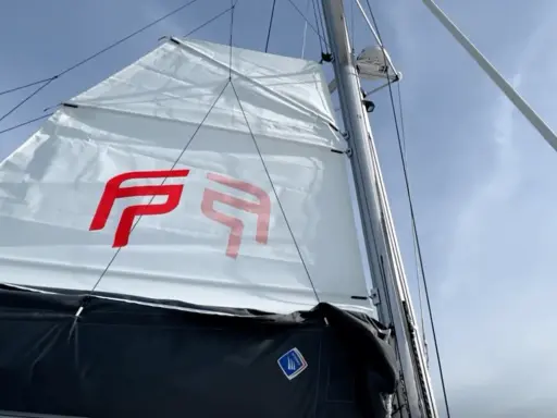 Voile blanche avec logo rouge, prête à naviguer à la voile sous un ciel bleu.