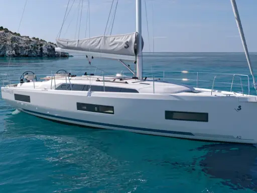 Un voilier blanc moderne navigue sur des eaux turquoise claires, près d'une île rocheuse. Ce modèle, le "Oceanis 42", pourrait bien être le meilleur voilier habitable pour vos aventures.