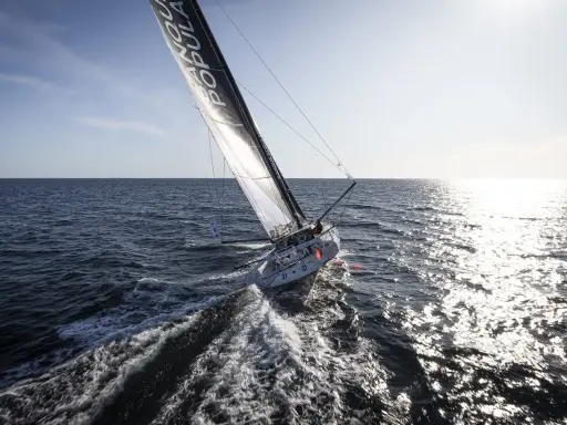 Voilier Banque Populaire naviguant au soleil, l'eau éclabousse le long du babord tribord.