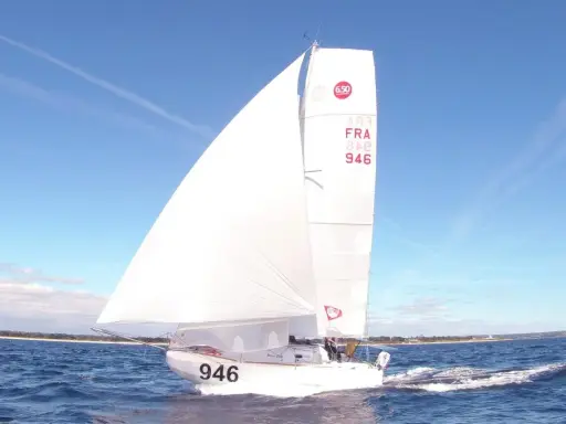 Un voilier de la classe mini, numéro 946, navigue sur une mer bleue sous un ciel clair.